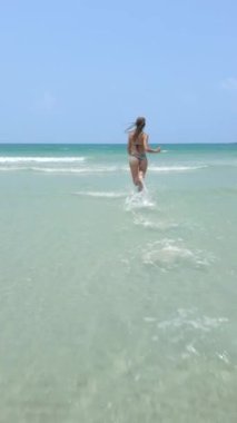 Mutlu genç kadın kristal berrak turkuaz suyun içinden okyanusa doğru neşeyle koşuyor. Yaz mevsimi, mutluluk, heyecan ve minnettarlık kavramları.