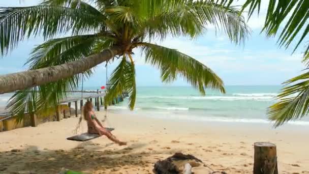 タイの熱帯のビーチで美しいヤシの木の上でスイングに揺れる若い女性 — ストック動画