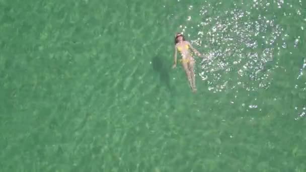 休暇中の澄んだ海水の中でリラックスして泳ぐ美しい若い女性のトップビュー — ストック動画