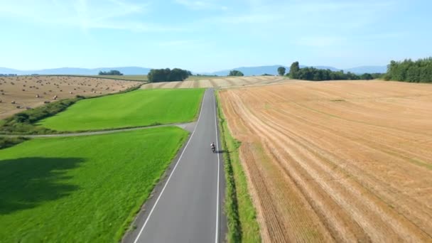 Fpv Drone Etter Motorsykkel Kjører Landevei Gjennom Felt Sommeren – stockvideo