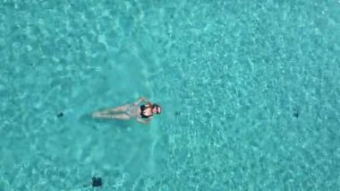 Genç bir kadının havuzda yavaş çekimde yüzüşünün üst görüntüsü..