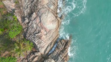 Okyanus dalgalarının üst görüntüsü kayalık tropikal kıyı şeridini vuruyor..