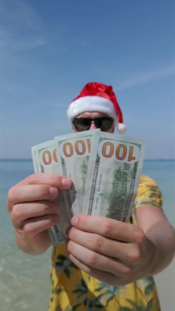 トロピカルビーチで米ドルを数えるサンタの帽子をかぶっている男 — ストック動画