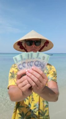 Vietnam şapkalı adam Vietnam 'da tropikal plajda Vietnam Dong' unu tutuyor. Kapat..