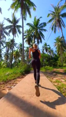 Kafkasyalı kadın Tayland 'da tropik adalarda palmiye ağaçları olan manzaralı bir yolda ağır çekimde koşuyor..