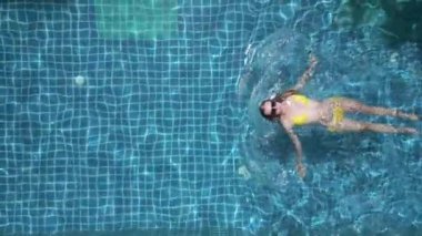 Ağır çekimde havuzda yüzen beyaz bir kadının üst görüntüsü..