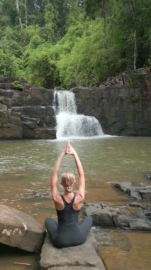 Beyaz kadın Tayland 'daki tropikal yağmur ormanlarındaki bir şelalede meditasyon yapıyor..