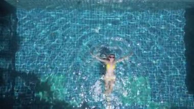 Ağır çekimde havuzda yüzen beyaz bir kadının üst görüntüsü.