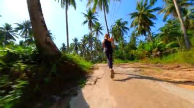 Kafkasyalı kadın Tayland 'da palmiye ağaçlarıyla tropikal yolda ağır çekimde koşuyor..