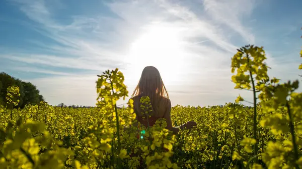 Güneş batarken sarı kolza tohumu tarlasında duran beyaz kadın.