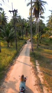 Tayland 'da tropik bir adada scooter süren beyaz bir kadın.