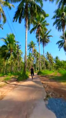 Formda bir kadın, Tayland 'da palmiye ağaçlarıyla tropikal yolda ağır çekimde koşar.