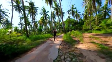 Formda bir kadın, Tayland 'da palmiye ağaçlarıyla tropikal yolda ağır çekimde koşar.