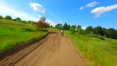 FPV insansız hava aracı yüksek hızda bir motokros pistinde yarışçıyı takip ediyor. Ekstrem spor, adrenalin ve yarış kavramları.