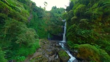 Endonezya 'da ormandaki çarpıcı tropikal şelalenin yumuşak FPV uçuşları