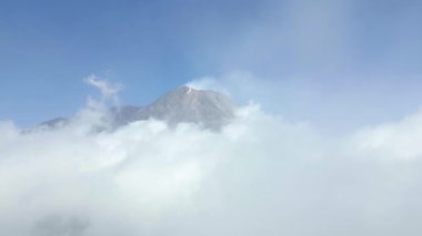 Mavi gökyüzündeki bulutların üzerindeki aktif Merapi volkanı, Endonezya.