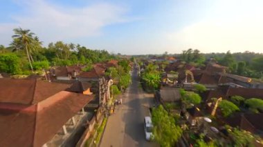 Ubud, Bali, Endonezya 'da düzenlenen Galungan tatili sırasında geleneksel köy üzerindeki sinematik FPV uçuşu.