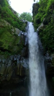 Central Java, Endonezya 'daki ormanda tropikal şelalenin sinematik FPV çekimi