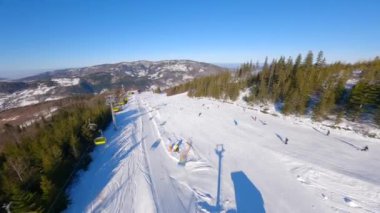 Güneşli bir günde dağlarda kayak ve snowboard yapan insanlarla kayak pistinde pürüzsüz bir FPV uçuşu.