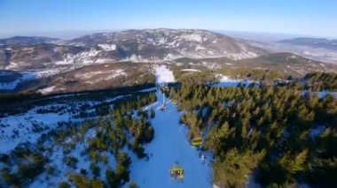 Dağın yamacındaki kayakçılar ve snowboardcularla asansörün üzerinden pürüzsüz bir FPV uçuşu.
