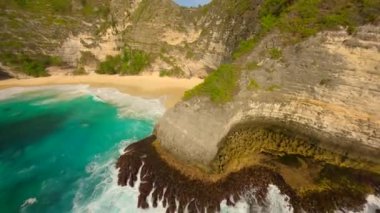 Endonezya, Bali 'deki Nusa Penida Adası' ndaki Kelingking Sahili boyunca yürüyen kadının sinematik FPV görüntüsü..