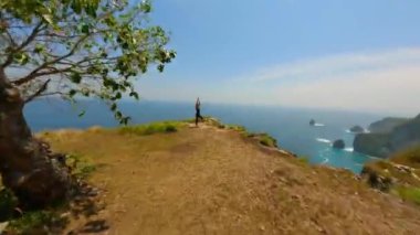 Endonezya 'daki Nusa Penida Adası' ndaki bir uçurumda yoga yapan atletik kadının sinematik FPV çekimi.