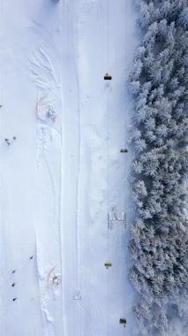 Bir teleferiğin havadan görünüşü ve insanlar kış dağlarında karlı bir yamaçta kayak yapıyor.
