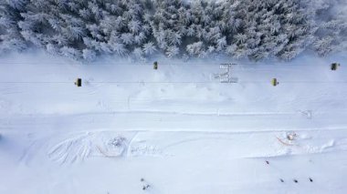 Bir teleferiğin havadan görünüşü ve insanlar kış dağlarında karlı bir yamaçta kayak yapıyor.