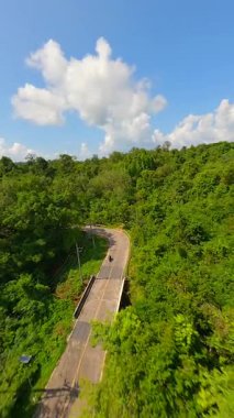 Tayland 'da güneşli bir günde tropikal ormanda motosiklet sürerken çekilmiş FPV görüntüleri.