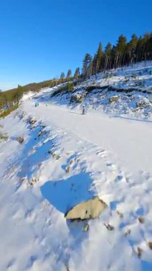 Güneşli bir günde kayak ve snowboard yapan insanlarla karlı dağ yamacında yumuşak bir FPV uçuşu.