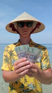 Vietnam şapkalı adam Vietnam 'da tropik plajlarda Vietnam Dong faturaları tutuyor.