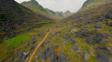 FPV 'nin insansız hava aracı Ha Giang dağlık arazisindeki kayalık dağ yolu üzerinde uçuyor.