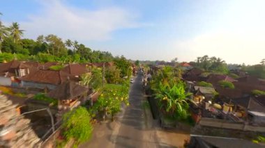 Endonezya 'nın Bali kentindeki bereketli tropik yeşilliklerle çevrili geleneksel Bali köyündeki süslü cadde üzerinde dinamik FPV insansız hava aracı uçuşu