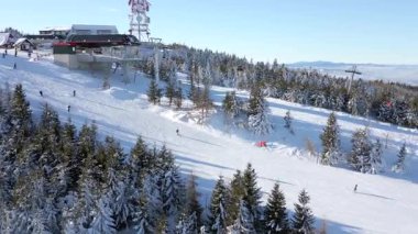 Güneşli bir kış gününde insanların yamaçta kayak yaptığı karlı kayak merkezinin hava manzarası..
