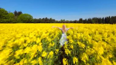 Güneşli bahar gününde sarı kolları açık atlayan bir kadının sinematik FPV drone görüntüsü. Tasasız kırsal yaşam tarzları özgürlük ve neşe teması için mükemmel..