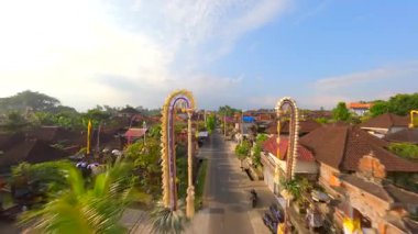 Endonezya 'nın Bali kentindeki bereketli tropikal yeşilliklerle çevrili geleneksel Bali köyündeki dekore edilmiş cadde üzerinde FPV insansız hava aracı uçuşu