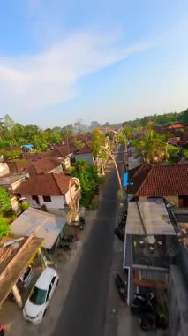 Endonezya 'nın Bali kentindeki bereketli tropikal yeşilliklerle çevrili geleneksel Bali köyündeki dekore edilmiş cadde üzerinde FPV insansız hava aracı uçuşu