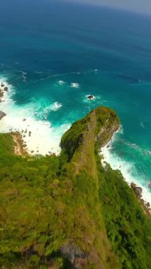 Endonezya, Bali 'deki Nusa Penida Adası' ndaki manzaralı uçurumlar ve turkuaz su boyunca sinematik FPV insansız uçuşu. Seyahat, doğa ve tropikal macera temaları için ideal hava manzarası.
