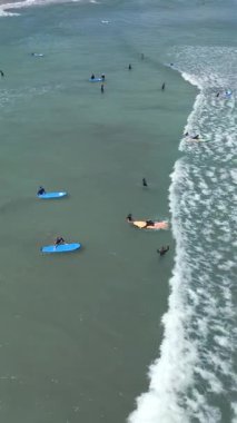 Endonezya, Bali 'de sörf derslerine katılan sörfçülerin küçük dalgalarda kürek çekmelerini ve sörf yapmalarını gösteren hava manzarası..