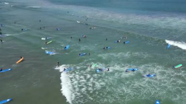 Endonezya, Bali 'de sörf derslerine katılan sörfçülerin küçük dalgalarda kürek çekmelerini ve sörf yapmalarını gösteren hava manzarası..