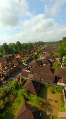 Endonezya 'nın Bali kentindeki bereketli tropik yeşilliklerle çevrili geleneksel Bali köyünde süslü caddelerde motosiklet sürerken çekilmiş FPV insansız hava aracı görüntüleri.. 