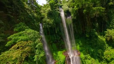 Endonezya 'nın Bali kentindeki yemyeşil ormanlarla çevrili Sekumpul Şelalesi' nin çağlayan sularında FPV insansız hava aracı uçuşu. Doğa, seyahat ve tropikal macera temaları için ideal.