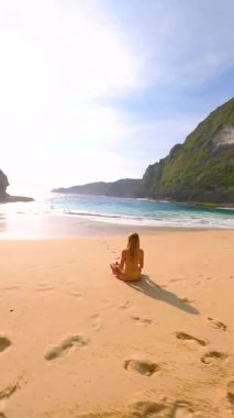 FPV 'nin uzaktan kumsalda tek başına meditasyon yapan kadın görüntüsü. Turkuaz deniz, dalgalar ve uçurumlar, Bali, Endonezya. Rahatlamanın, farkındalığın ve iç huzurun huzurlu sahnesi..