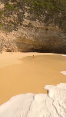 Endonezya, Bali 'deki boş tropik plaj boyunca sarı mayo içinde koşan kadının sinematik FPV görüntüsü. Yaşam tarzı, özgürlük, seyahat, yaz, sağlık ve macera temaları için mükemmel.