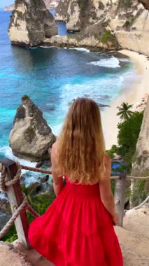 Endonezya, Bali 'deki Nusa Penida Adası' ndaki Elmas Sahili 'nin manzaralı uçurumlarını ve turkuaz sahillerini keşfeden bir kadın. Seyahat, macera, özgürlük ve tropikal güzellik temaları için ideal.