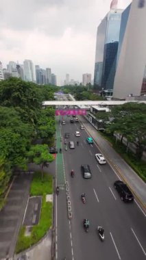 Jakarta, Endonezya 'nın merkez ticaret bölgesinde sabah trafiği, otobüs durağı ve motosiklet şeritleri olan yoğun çoklu şeritli bir cadde üzerinde FPV insansız hava aracı uçuşu. Ulaşım ve altyapı temaları için ideal.