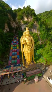 Malezya 'daki Batu Mağaraları' nda altın Murugan heykeli etrafında dönen sinematik FPV insansız hava aracı. Rengarenk merdivenleri, kireçtaşı uçurumları ve yemyeşil alanları seyahat ve kültürel temalar için idealdir..