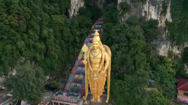 Malezya 'daki Batu Mağaraları' ndaki altın Murugan heykelinin havadan görünüşü. Rengarenk merdivenleri, kireçtaşı uçurumları ve yemyeşil alanları seyahat ve kültürel temalar için idealdir..