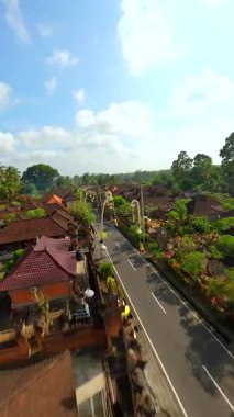 Endonezya 'nın Bali kentindeki bereketli tropikal yeşilliklerle çevrili geleneksel Bali köyündeki dekore edilmiş cadde üzerinde FPV insansız hava aracı uçuşu