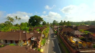 Endonezya 'nın Bali kentindeki bereketli tropikal yeşilliklerle çevrili geleneksel Bali köyündeki dekore edilmiş cadde üzerinde FPV insansız hava aracı uçuşu